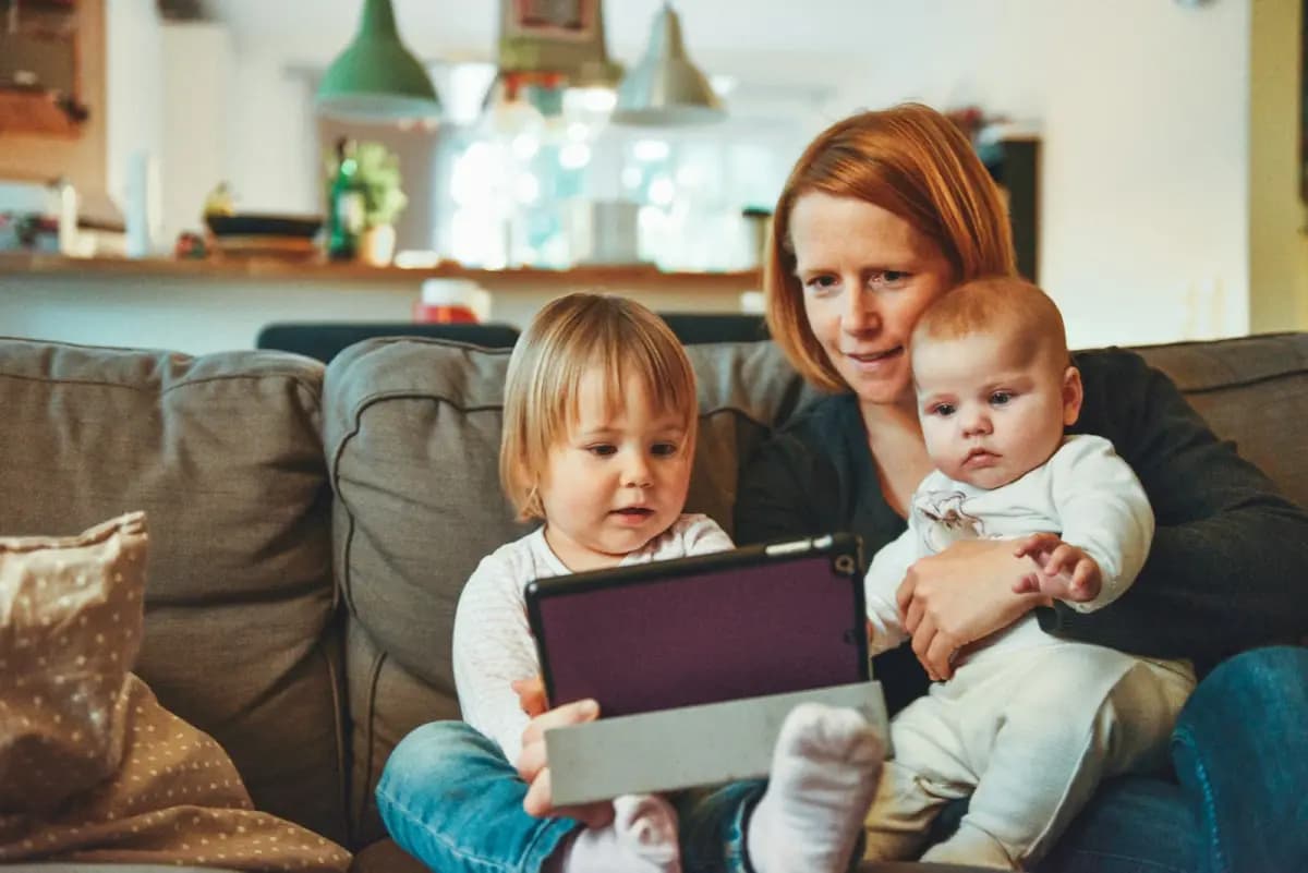 A mother and her two children consult a tablet in their living room